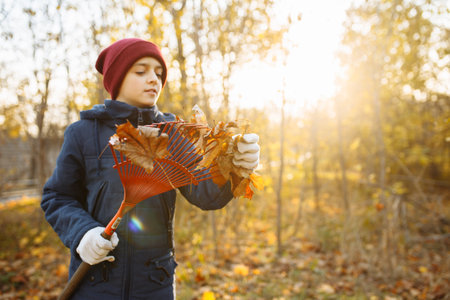 A young man gathers leaves in a woodland or park. A male volunteer engages in cleanup amidst the...