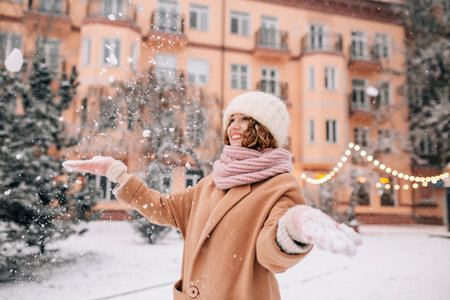 Portrait of smiling middle aged woman shaking off snow from her gloves. Close shot of smiling girl playing with snow outside in the city park in winterの写真素材