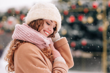 A snowy cityscape with a young woman wearing winter attire, posing in front of the Christmas tree. A winter scene with falling snowの写真素材