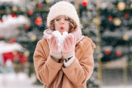 Portrait of a curly-haired girl playing in the snow. A woman blows snow on a beautiful winter dayの写真素材