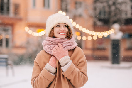 A joyous girl poses in the park amidst fir trees and twinkling lights on a stunning snowy winter day. Close-up of a woman in an urban sceneの写真素材