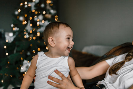 A close-up shot of a happy little boy against the backdrop of a Christmas tree. The child is at home in a cozy festive atmosphere. Winter holidays and people conceptの写真素材