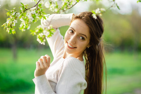 A close-up shot of a beautiful girl with long hair posing in a blooming park among the trees in spring. The concept of femininity, happiness and loveの写真素材