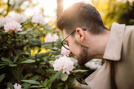 A young stylish man smells spring flowers in the park at sunset on a sunny day. Spring time. Relaxation, youth, lifestyle solitude with natureの写真素材