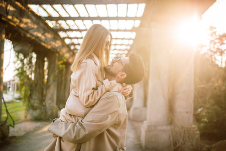 Close-up shot of a beautiful couple posing in a park garden on a spring sunny day. A man holds a woman in his arms. Family, love and happiness conceptの写真素材