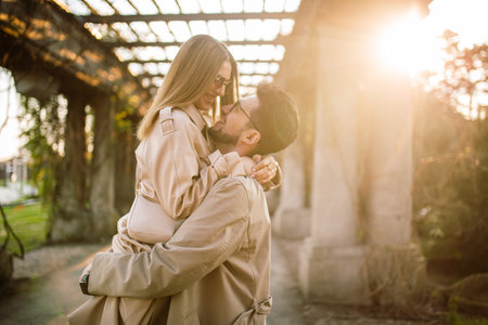 Close-up shot of a beautiful couple posing in a park garden on a spring sunny day. A man holds a woman in his arms. Family, love and happiness conceptの写真素材