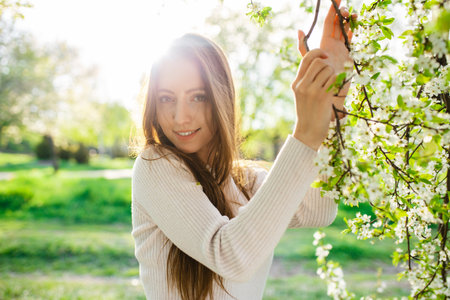A stunning woman with long hair posing in a spring garden during sunset on a beautiful sunny day....