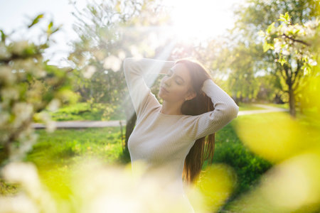 A young beautiful woman relaxes in a wonderful blooming spring garden at sunset. The concept of calm, femininity and happinessの写真素材