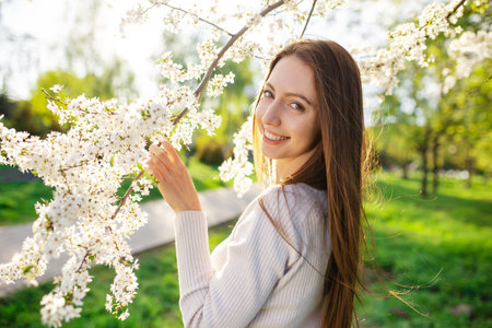 Portrait of a charming laughing woman in a beautiful dress posing near a blooming apple tree in an...