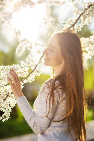Portrait of a woman in a beautiful dress posing next to a flowering tree in a autumn park at sunset. The concept of femininity, happiness and loveの写真素材