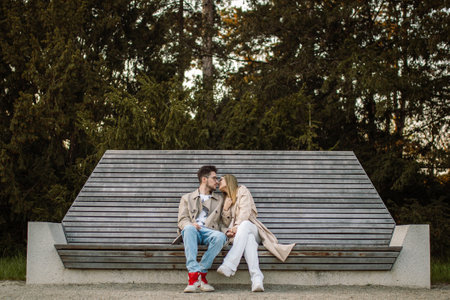 Beautiful stylish young couple sitting on a bench. A woman and a man are talking and enjoying time and spring weather togetherの写真素材