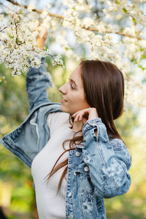 A young woman enjoying herself in a fragrant garden filled with blooming apple and cherry trees during the spring at sunset. The concept of femininity, happiness and loveの写真素材