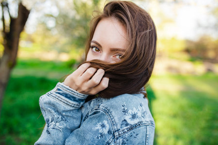 Close-up shot of a young woman enjoying herself in a fragrant garden filled with blooming apple and cherry trees during the spring at sunset. A girl playing with her hairの写真素材