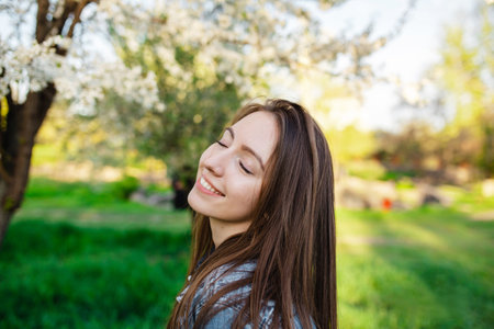 Portrait of a handsome smiling with teeth girl in a spring garden at sunset. A woman relaxes in a park with blooming apple and cherry treesの写真素材