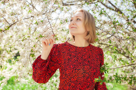 Charming cute woman posing in flowers in a blooming garden park on a sunny spring day against the backdrop of a green field. The concept of unity with natureの写真素材