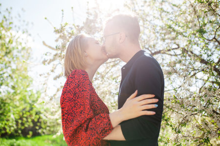 A stylish beautiful couple kisses and hugs against the backdrop of a flowering tree on a sunny spring dayの写真素材