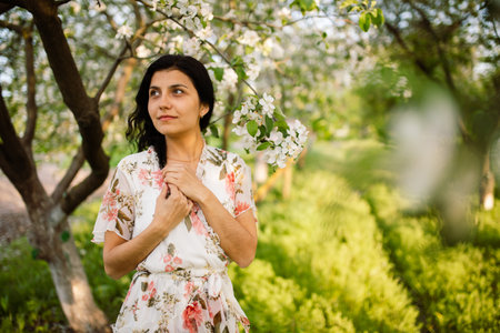 Young woman wearing stylish outfit near blossoming cherry apple trees. Nude makeup. Close up portraitの写真素材