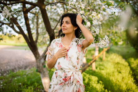 Young woman wearing stylish outfit near blossoming cherry apple trees. Nude makeup. Close up portraitの写真素材