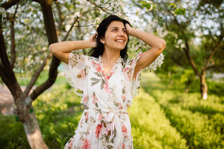 Close-up shot of a brunette woman posing in a blooming garden on a beautiful spring day. Concept of happiness, relaxation and loveの写真素材