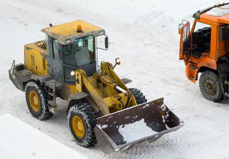 the tractor loads the cleaned snow on the dump truck