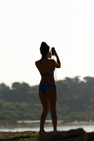 girl on the beach in a swimsuit with a phoneの写真素材