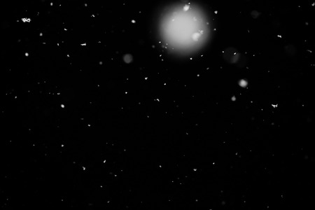 Snowstorm texture. Bokeh lights on black background, shot of flying snowflakes in the airの写真素材
