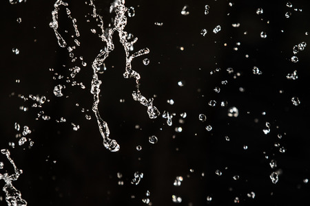 Water splash in dark with a drops of water flying, defocused bokeh.の写真素材