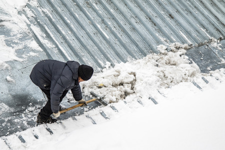 A man removes snow shovel top view, metal roof.の写真素材