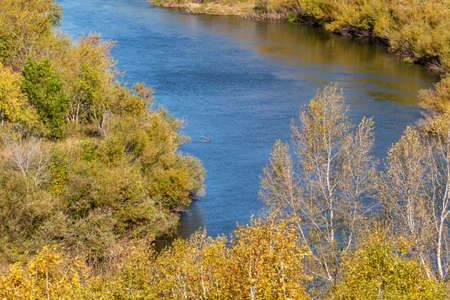 Autumn landscape, yellow trees, dead grass, blue river. Sunny autumn day.