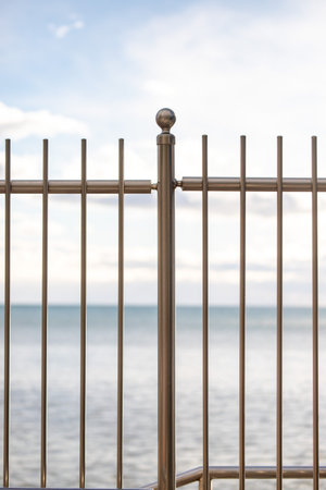 metal fence on the background of the sea and blue sky with cloudsの写真素材