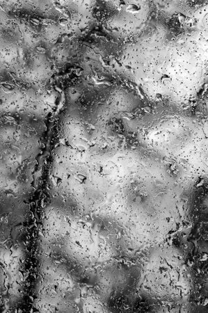 A blurry image of raindrops on a window. The image has a moody and somewhat melancholic feel to it, as the raindrops are scattered and blurred, creating a sense of movement and chaosの写真素材