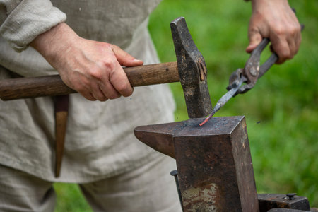 A man is hammering a piece of metal. Concept of hard work and dedication, as the man is focused on his task. The metal piece being worked on could be a piece of jewelry or a toolの写真素材