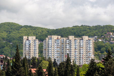 A large building with a lot of windows is seen from a distance. The building is surrounded by trees and mountainsの写真素材
