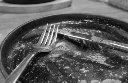 A dirty plate with a fork and knife on it. The plate is black and the utensils are silver. Scene is somewhat sad or melancholic, as the dirty plateの写真素材