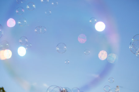 A bunch of bubbles are floating in the air, creating a colorful and playful atmosphere. The sky is clear and blue, providing a perfect backdrop for the bubbles. Concept of joy and freedomの写真素材