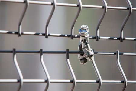 A bolt is hanging from a fence. The bolt is silver and has a nut on topの写真素材
