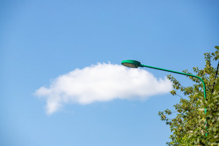 A green street light is lit up in the sky. The light is shining on a cloud that looks like a person. The sky is clear and blue, and the light is casting a shadow on the treeの写真素材