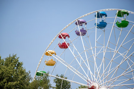 A colorful carousel with many different colored seats. The carousel is in the middle of a park with trees in the backgroundの写真素材