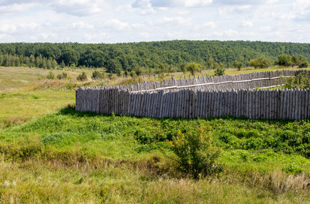 A wood fence surrounds a field of grass. The fence is made of wood and is tall. The grass is green and the sky is blueの写真素材
