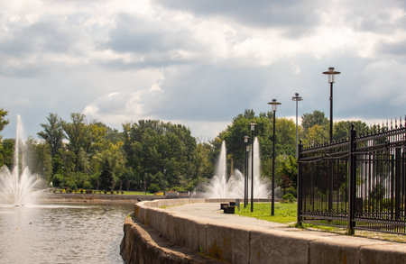 A park with a fountain and a fence. The fountain is on the left side of the image and the fence is on the right sideの写真素材