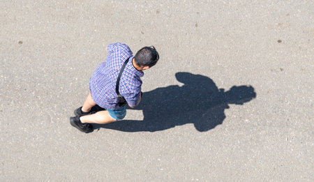 A man is walking down a street wearing a blue shirt and shorts. He is carrying a backpack and a handbagの写真素材