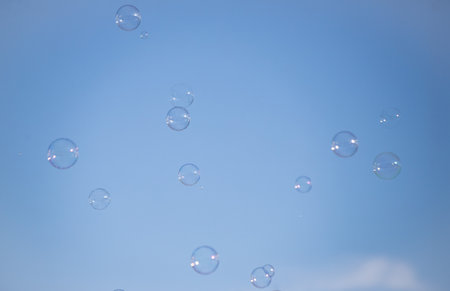 A bunch of bubbles floating in the sky. The bubbles are of different sizes and are scattered all over the sky. The sky is clear and blue, and the bubbles are reflecting the sunlightの写真素材