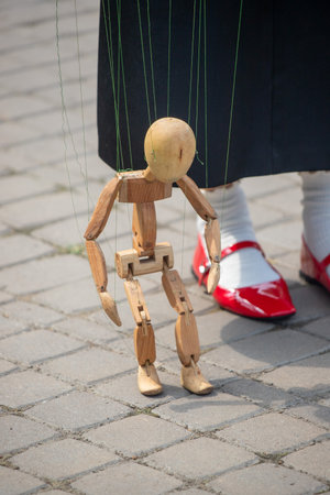 A wooden puppet is being held by a woman in a red shoe. The puppet is dressed in black and he is a puppet of a person. The woman is standing on a brick sidewalkの写真素材