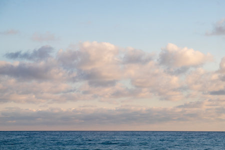 A large cloud is floating over the ocean. The sky is clear and blue, and the water is calm. The scene is peaceful and serene, with the cloud providing a sense of depthの写真素材