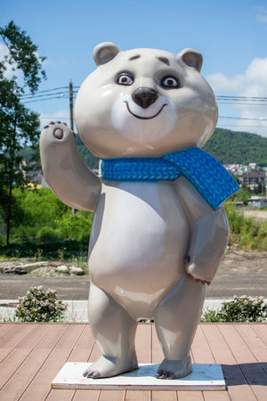A large bear statue with a blue scarf is standing on a sidewalk. The bear is smiling and waving, giving the impression of a friendly and welcoming presence. The blue scarf adds a touch of colorの写真素材