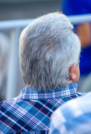 A man with a plaid shirt and a gray head. The man is sitting downの写真素材