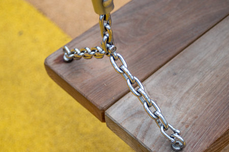 A chain is attached to a wooden bench. The chain is attached to a metal object. The bench is on a yellow surfaceの写真素材