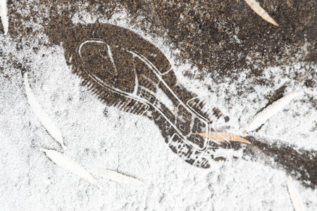 A shoe print is in the snow. The snow is white and the ground is gray. The image has a peaceful and serene moodの写真素材
