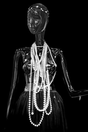 A mannequin wearing a black dress and a necklace of pearls. The necklace is long and has many pearlsの写真素材