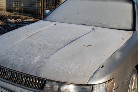 A car with a dirty windshield and a snow covered hood. The car is parked in a drivewayの写真素材